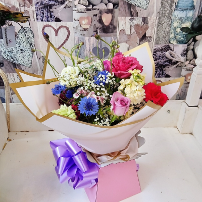 Rose cottage romance - A joyful hand-tied bouquet featuring a beautiful blend of pastel shades with vibrant pops of colour, accented by delicate seasonal blooms and fresh greenery. Wrapped in luxurious presentation paper and finished with a statement ribbon