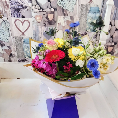 Festival of Colour - A joyful, vibrant arrangement bursting with a lively mix of bold and cheerful colours, beautifully balanced with fresh greenery. Presented in stylish gold-edged wrapping and a striking purple gift box, this eye-catching design is perfect for birthdays, celebrations, thank-you gestures, or simply brightening someone’s day.