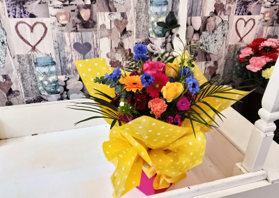 Sunshine Celebration - A bright and joyful arrangement overflowing with vivid shades of yellow, orange, pink, blue and rich berry tones, complemented by fresh greenery. Presented in cheerful yellow polka-dot wrapping, this vibrant design is perfect for birthdays, congratulations, thank-you gifts or simply sending a burst of happiness to someone special.