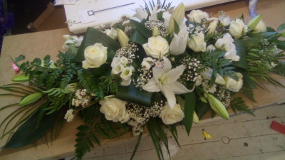 Pure Grace - A serene and elegant sympathy arrangement designed in timeless white and ivory tones, beautifully complemented by lush, flowing greenery. Its graceful, natural shape creates a peaceful and dignified tribute, offering a heartfelt expression of love, remembrance and respect.