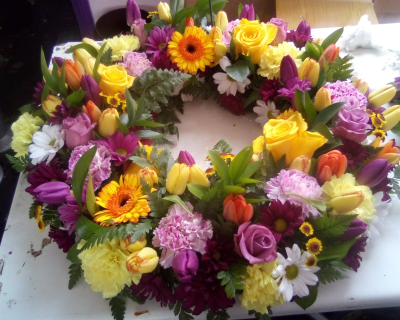 Vibrant Wreath - A vibrant and uplifting circular tribute bursting with joyful shades of yellow, orange, purple, pink and white, complemented by fresh greenery. Full of warmth and colour, this beautiful wreath offers a heartfelt way to celebrate a life filled with love, happiness and treasured memories.